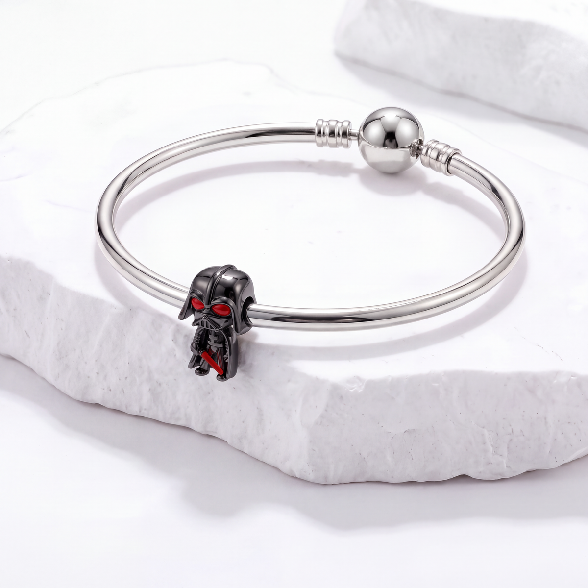 Star Wars charms featuring a Darth Vader helmet charm on a silver bracelet against a white stone background.