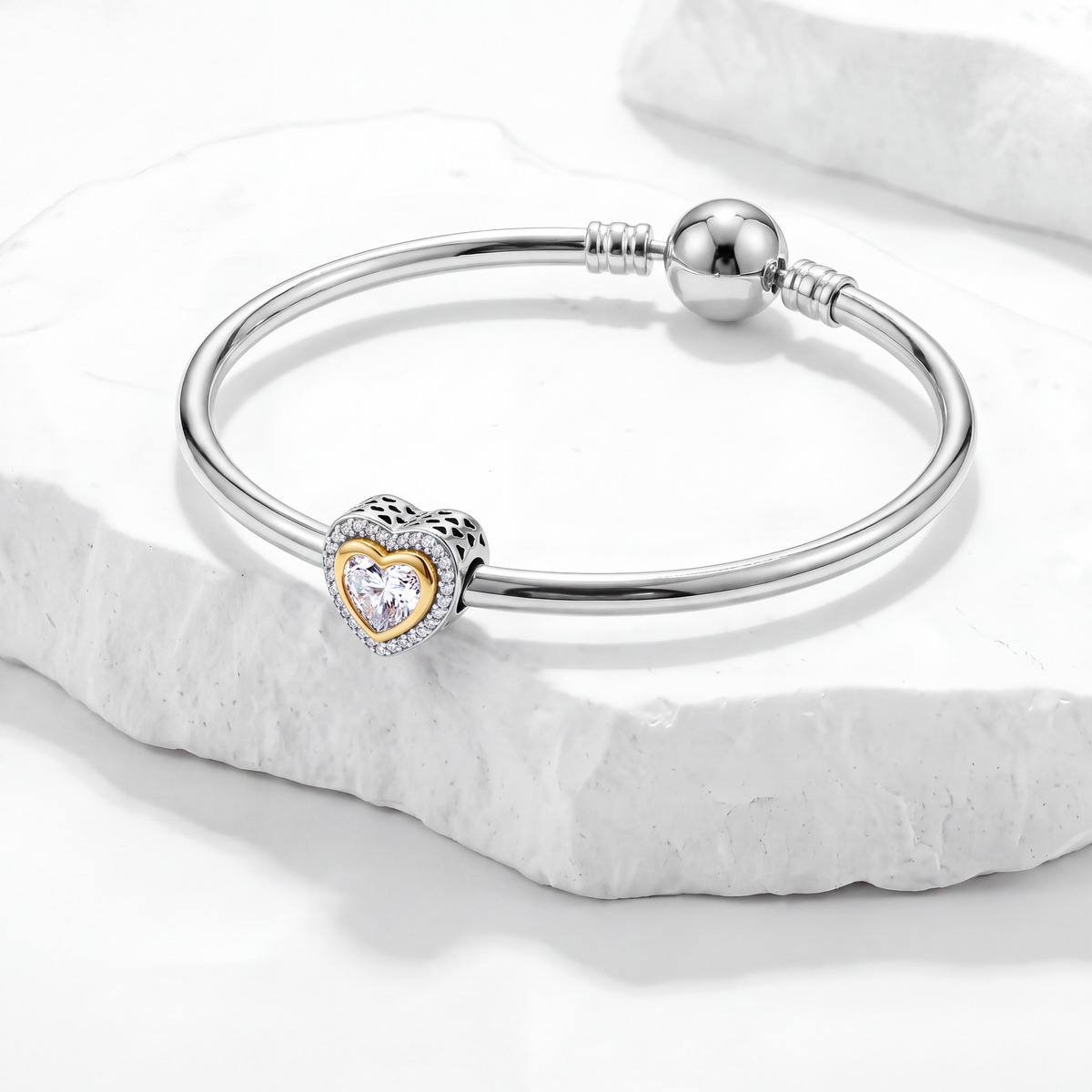 Sparkle charms silver bracelet featuring a heart charm with a golden outline and sparkling stone on a marble surface.