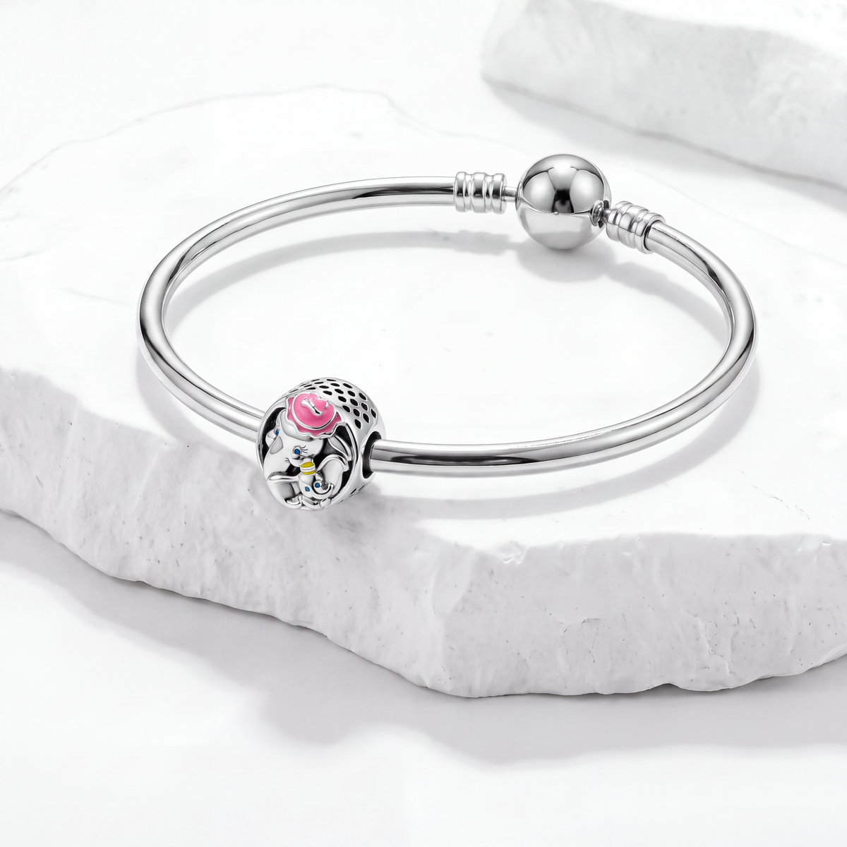 Dumbo Disney charms bracelet featuring a colorful Dumbo charm on a silver bangle against a marble background.