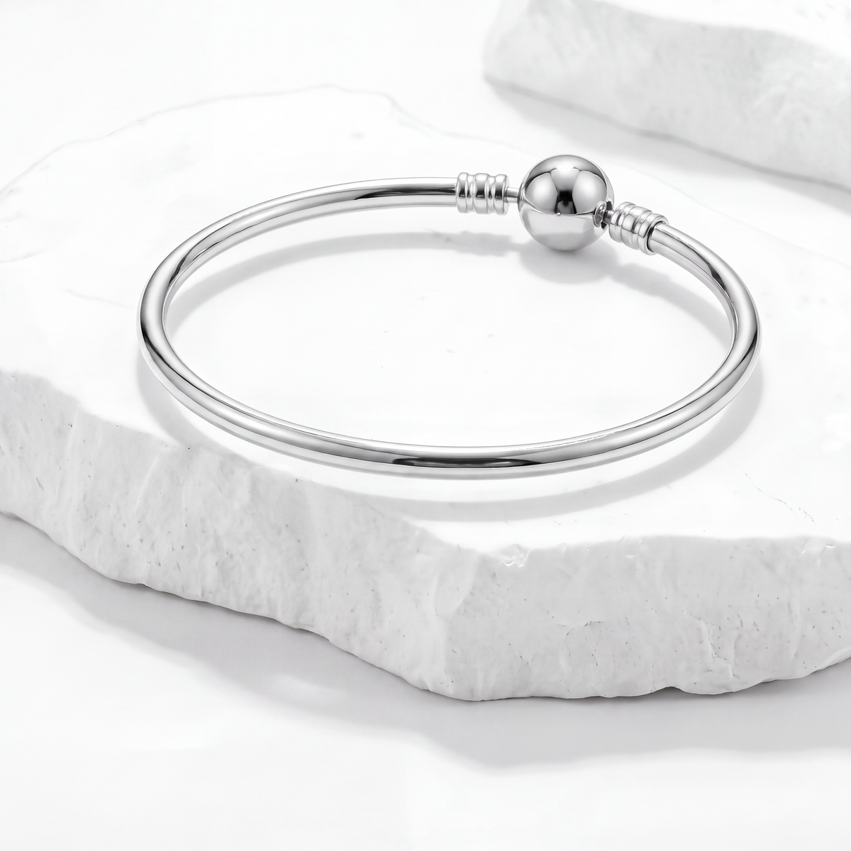 Elegant silver bracelet displayed on a white marble surface, perfect for charm and fashion bracelets.