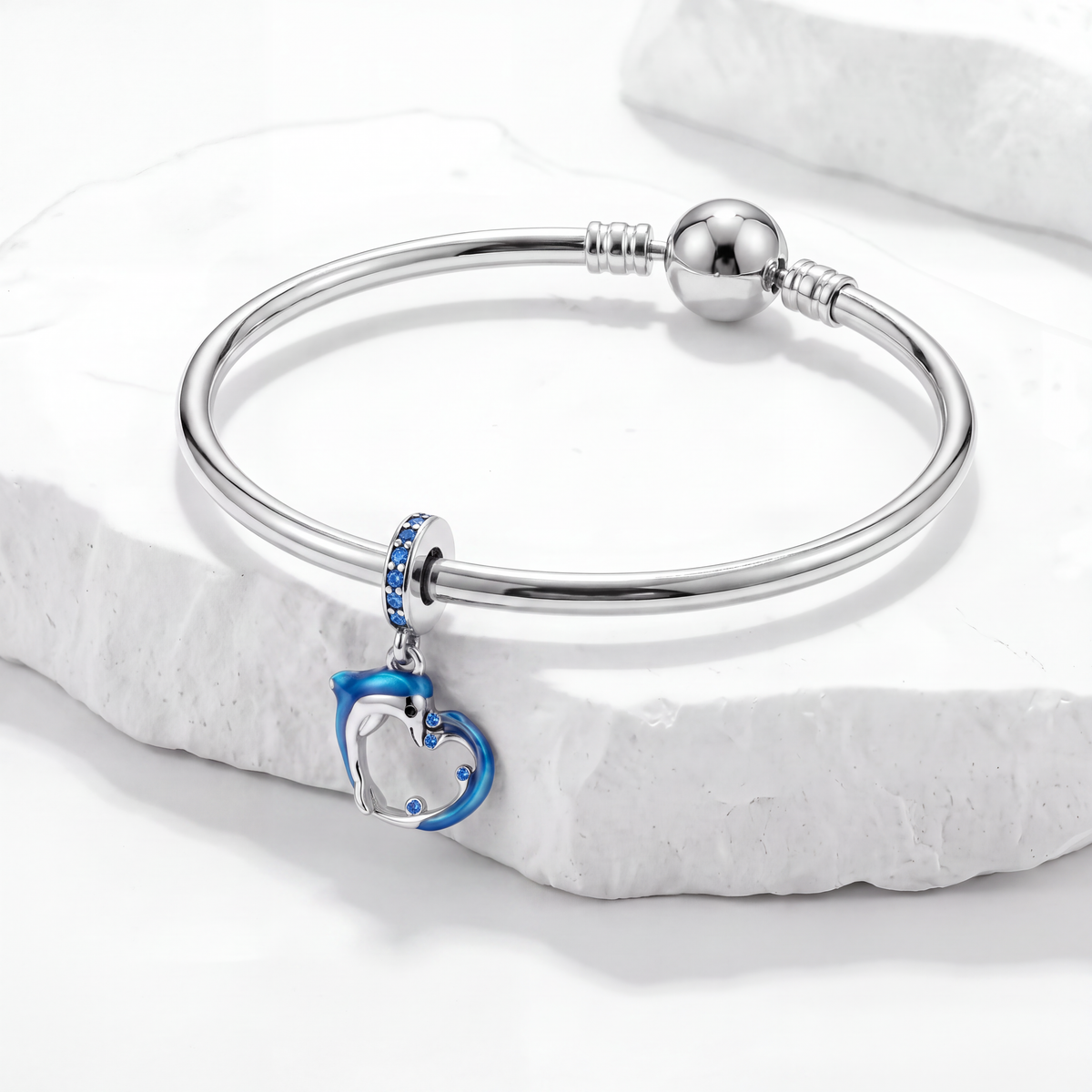 Ocean charms bracelet featuring a dolphin heart pendant and blue accents on a white marble surface.