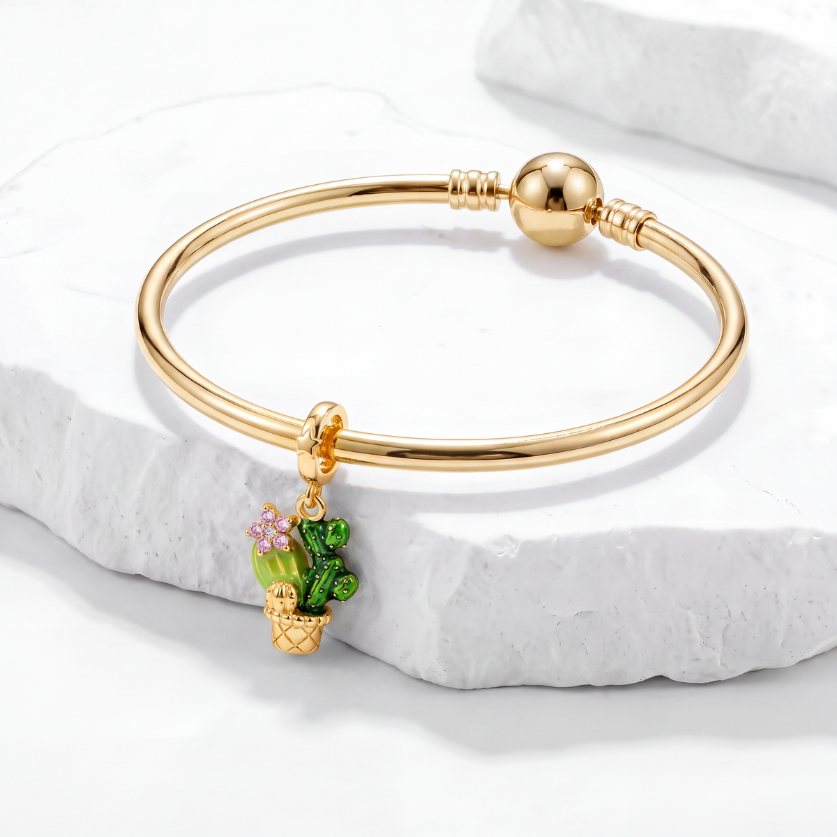 Gold bracelet with cactus charm from Our Latest Products collection on white marble.