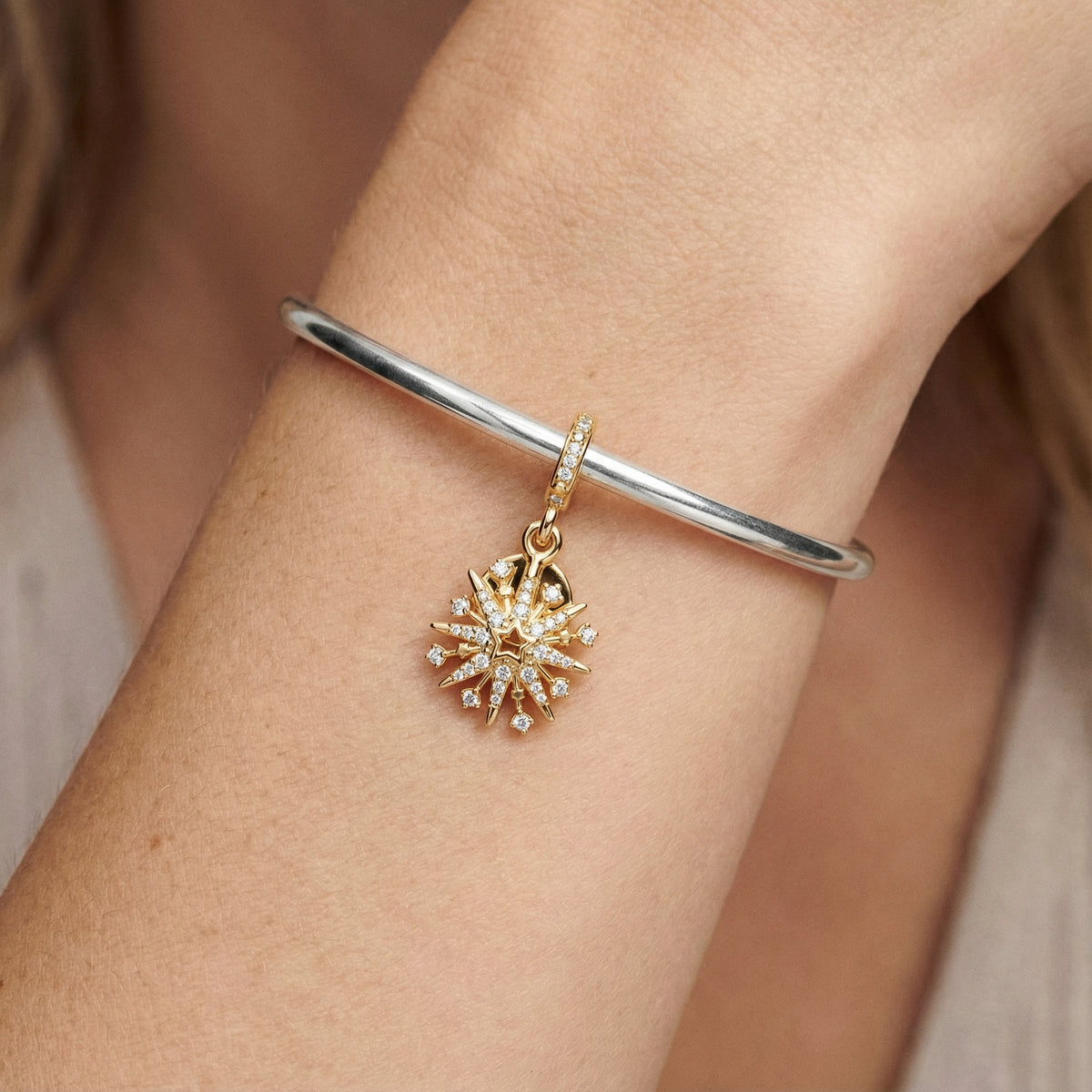 Golden Sparkling Starburst Pendant on a silver bracelet shining elegantly.